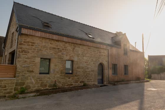 Façade en pierre et bardage bois doré par le soleil couchant